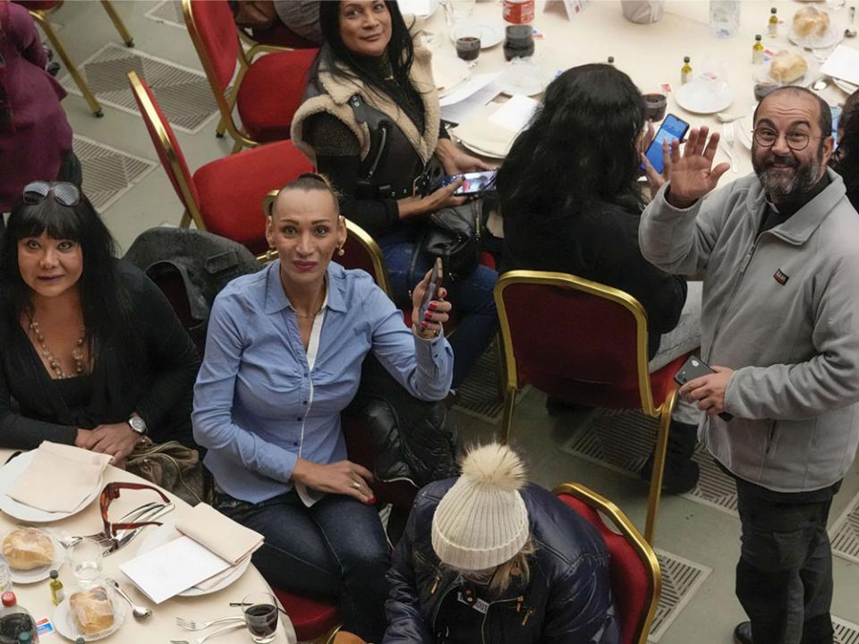 Don Andrea Conocchia, right, waves as he stands next to a table with a group of transgender women he accompanied at a lunch for the poor with Pope Francis, in the Paul VI Hall at the Vatican, Sunday, Nov. 19, 2023. Pope Francis offered several hundred poor people, homeless, migrants, unemployed a lunch on Sunday as he celebrates the World Day of the Poor with a concrete gesture of charity in the spirit of his namesake, St. Francis of Assisi. Photo by Andrew Medichini, Associated Press.